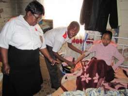 Two members of the care team attend to a seated woman during a home visit.