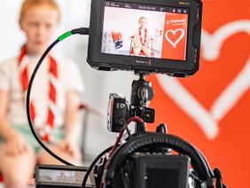 Ein Kind der Malteser Jugend wird vor einem Malteser-Logo fotografiert.