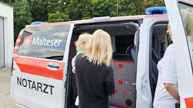 Eine Frau mit einem Kind auf dem Arm schaut in ein Notarzt-Auto.