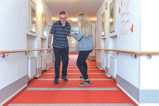 Ein Mann läuft mit Unterstützung einer Frau am Arm einen gang entlang