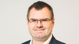Businessporträt einer Person mit Brille im Anzug vor hellem Hintergrund.