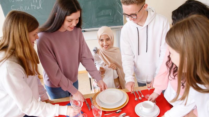 Eine Gruppe junger Menschen deckt gemeinsam einen Tisch ein.