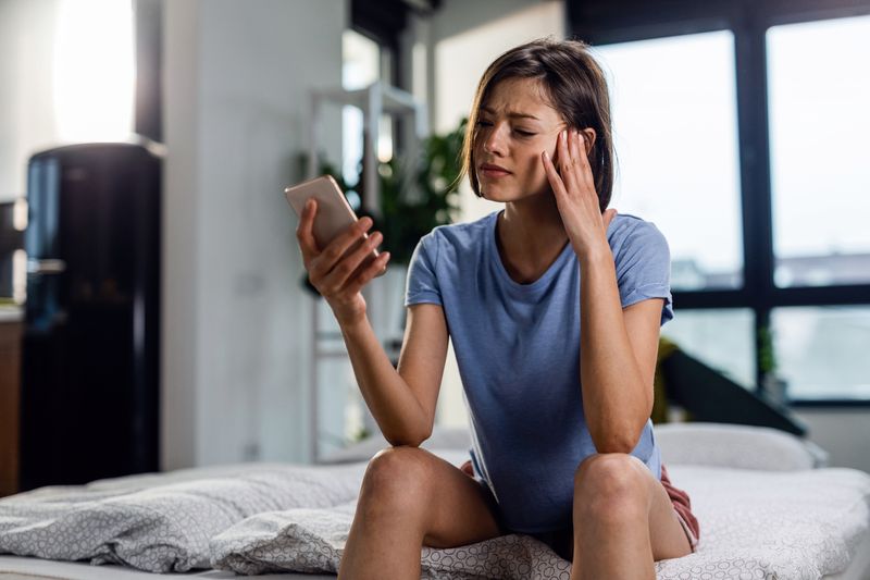 Frau sitzt im Bett und schaut aufs Handy