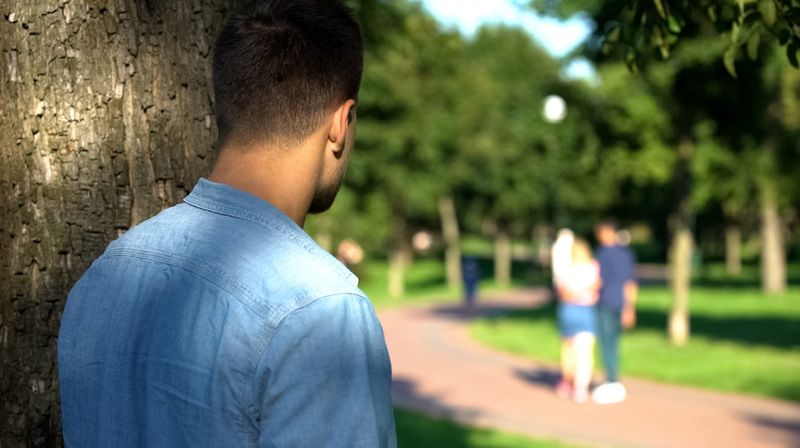 Junger Mann hinter einem Baum beobachtet ein Pärchen 