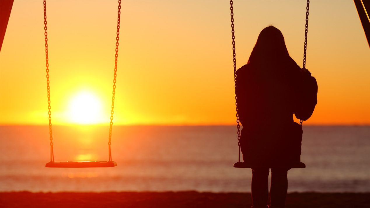 Eine Frau sitzt auf einer Schaukel und schaut in den Sonnenuntergang.