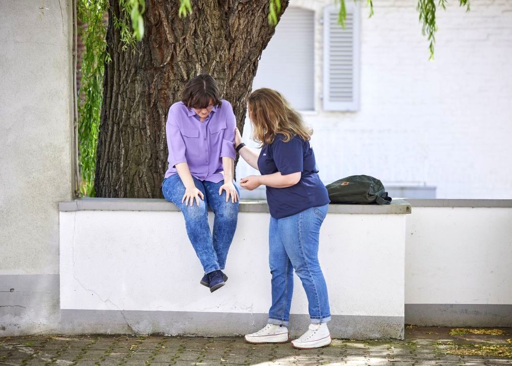 Eine Frau wendet sich einer anderen, wohl traurigen Frau tröstend zu.