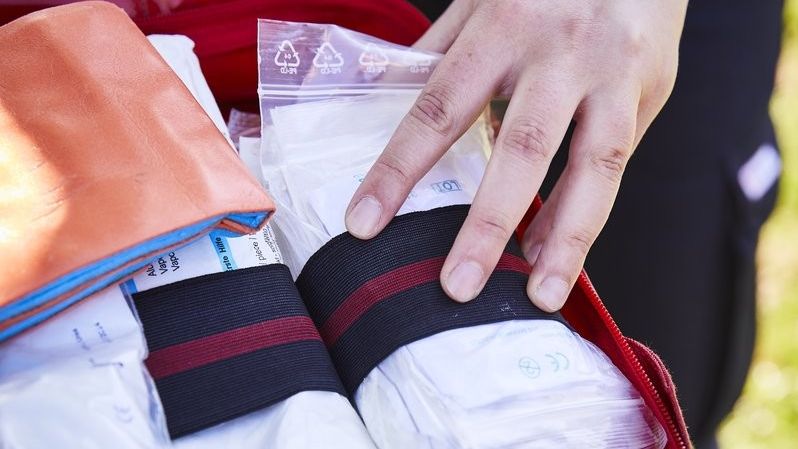 Eine Hand greift nach dem Inhalt eines geöffneten Erste-Hilfe-Sets.