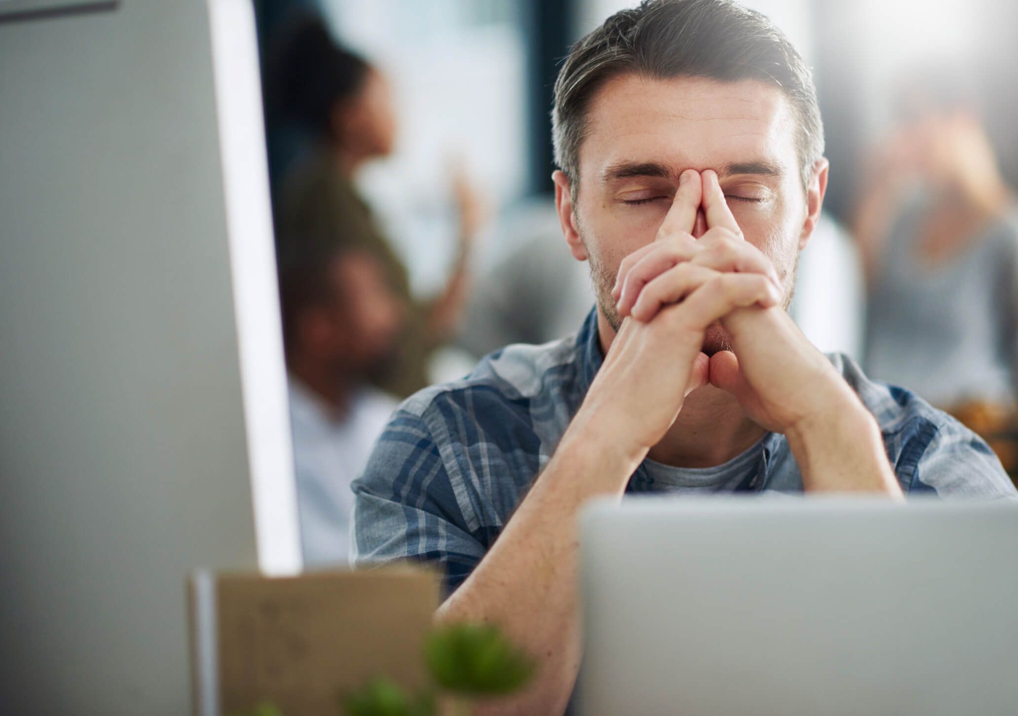 Junger Mann sitzt vor dem Computer und hält die Hände vor dem Kopf