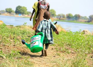 Ein Kind im Süd Sudan mit einer Gießkanne auf einem Feld