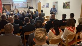 Thomas Haas, Leiter Einsatzdienste der Malteser Bayern, am Pult, geladene Gäste und Malteser sitzen in mehreren Reihen 