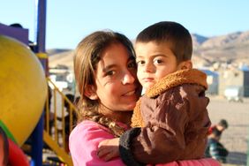 Eine junge irakische Mutter trägt ihren Sohn vor einem Spielplatz in Dohuk auf dem Arm.