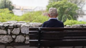 Älterer Mann sitzt mit dem Rücken zur Kamera auf einer Parkbank.