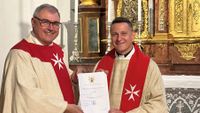 Domkapitular Hans-Georg Platschek und Prodekan Fabian Orsetti, beide mit liturgischem Gewand und Stola mit Malteserkreuz, halten gemeinsam eine Urkunde. 