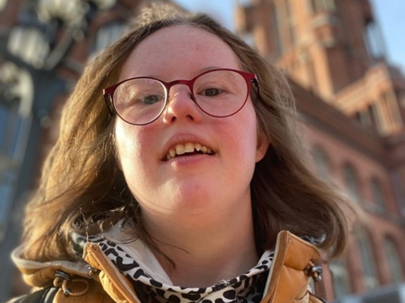 Junge Frau mit Brille vor einem rötlichen Gebäude