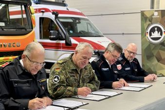 Vier Männer sitzen an einem Tisch und unterschreiben einen Vertrag. 