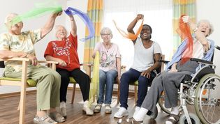 Fünf Frauen winken mit Tüchern und sitzen auf Stühlen.