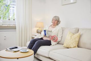 Ältere Dame auf der Couch mit Notrufarmand