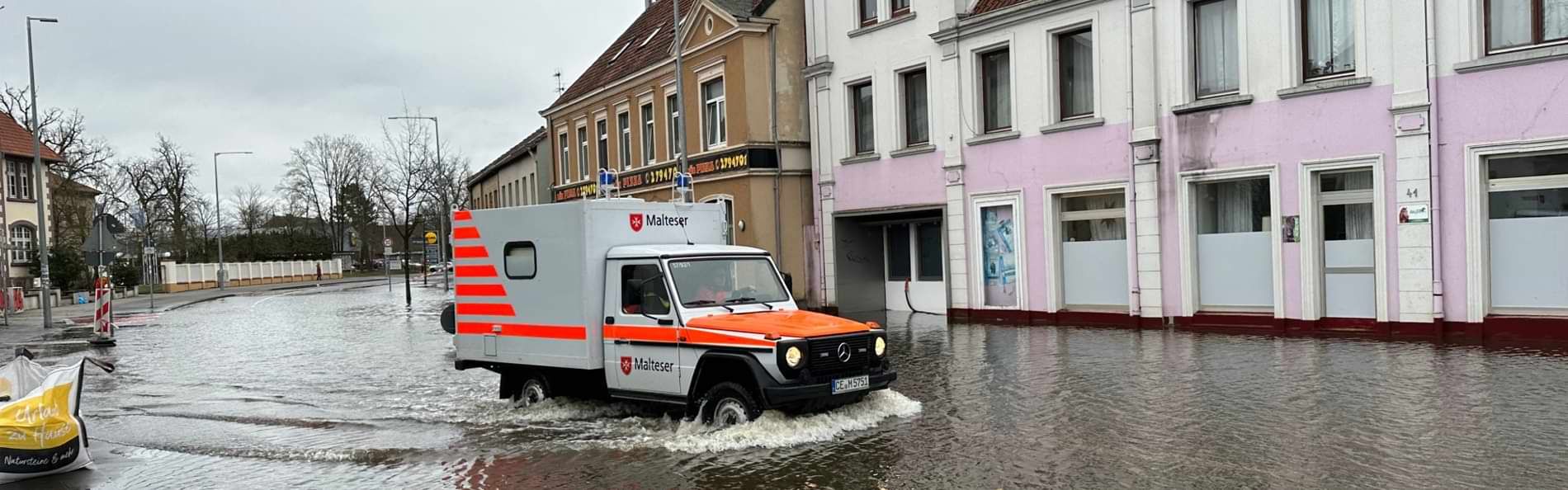 Ein Geländekrankenwagen der Malteser fährt über eine überschwemmte Straße