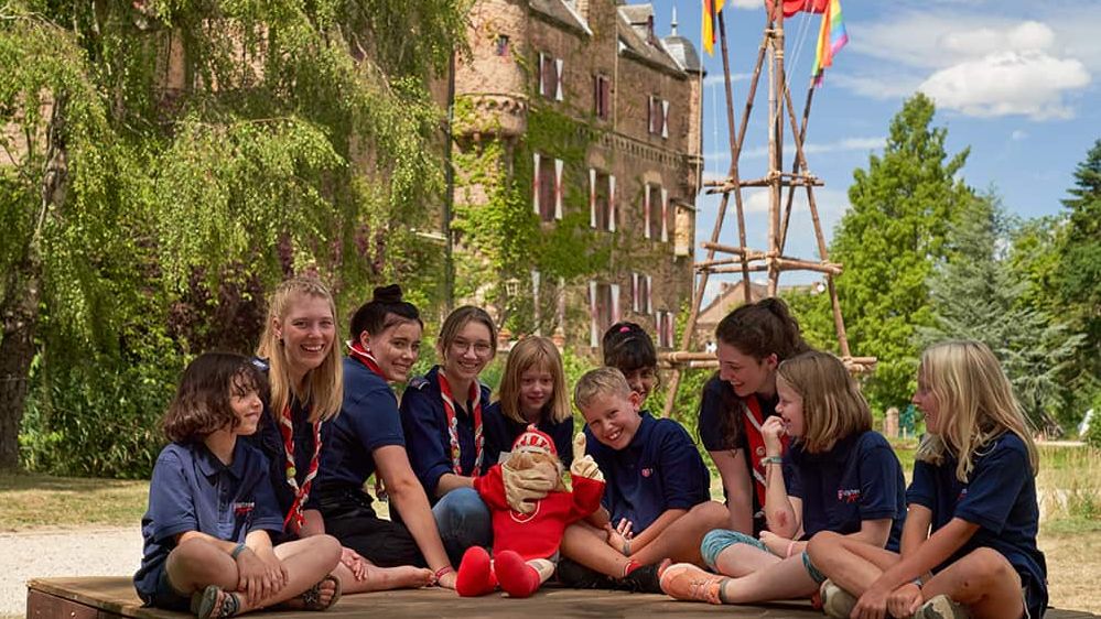 Beim Bundeslager der Malteser Jugend sitzt ein Gruppe von Kindern im Malteser Shirt vor einer Burg.