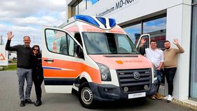 Vier Personen stehen neben einem ausgemusterten Rettungswagen.