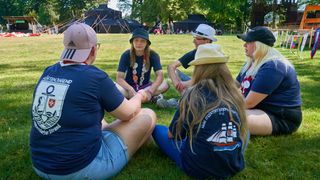 Ehrenamtliche der Malteser Jugend sitzen im Ferienlager im Freien zusammen.