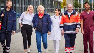 Malteser Mitarbeitende laufen gemeinsam durch den Innenhof eines Bürokomplexes.