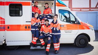 Eine Gruppe von Menschen im Freiwilligendienst in Einsatzkleidung am Rettungswagen. 