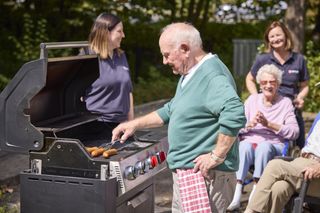 Mann am Grill und Personen die lachen im Hintergrund
