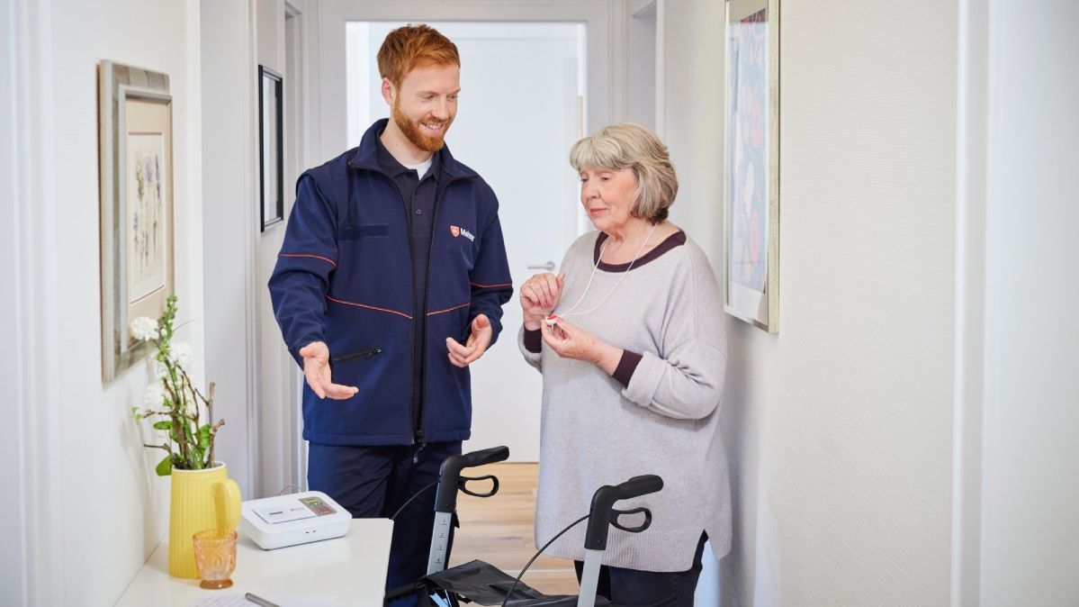 Ein Kundenbetreuer der Malteser installiert das Hausnotrufgerät bei einer älteren Frau zu Hause.
