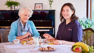 Eine junge und eine ältere Frau sitzen am Tisch und essen Kuchen.