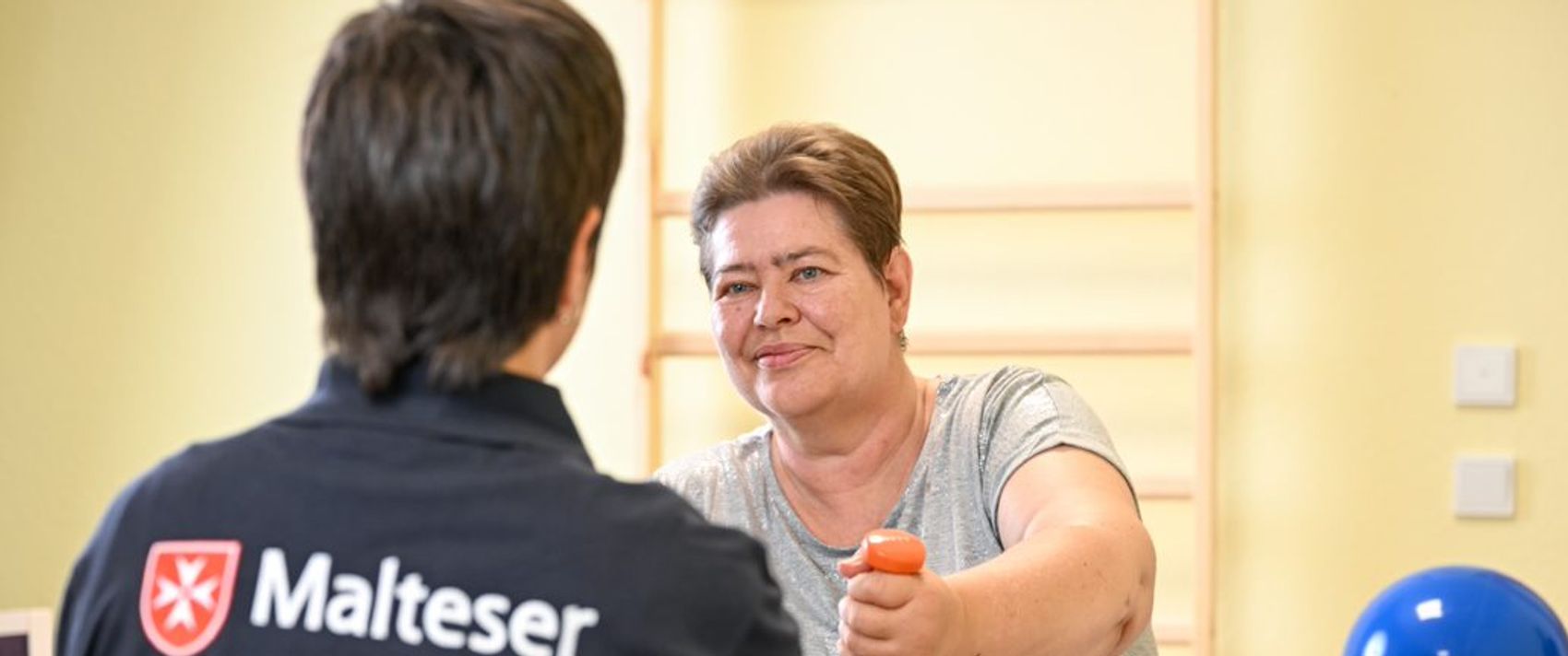 Eine Pflegerin im Malteser Shirt beim Training mit einer Patientin mit Hanteln