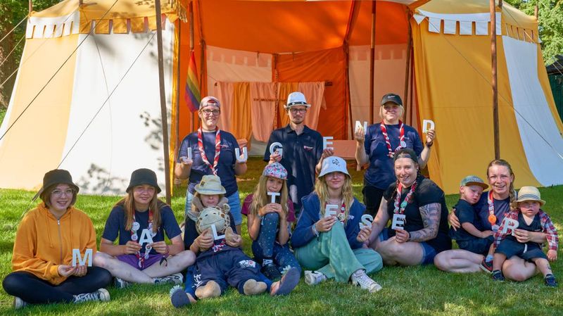 Junge Menschen und Kinder auf einer Wiese vor einem orangefarbenen Zelt
