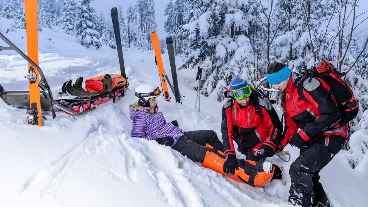 Zwei Bergretter versorgen das Bein einer jungen Skifahrerin.