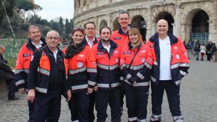 Männer und Frauen in Malteser Einsatzkleidung stehen vor dem Kolosseum in Rom. 