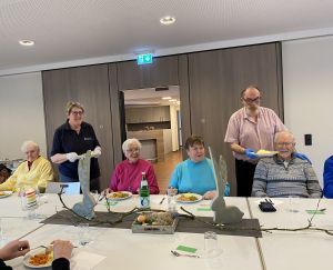 Malteser Helfer servieren den Gästen die Hauptmahlzeit am dekorierten Tisch