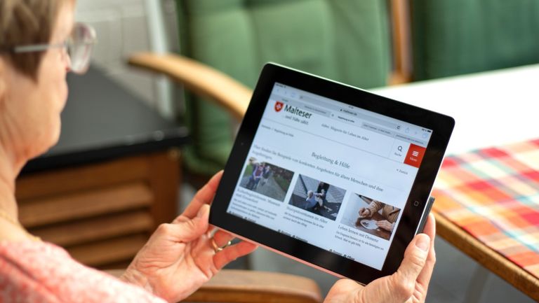 Älter Frau hält ein Tablett in den Händen und schaut auf den Bildschirm.