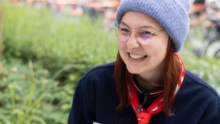 Junge Frau in Malteser Kleidung mit einer grauen Mütze sitzt im Freien an einer Schreibmaschine