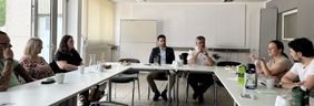  Zu sehen sind alle Beteiligten des Gesprächs an Tischen sitzend.