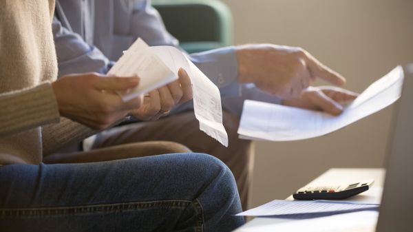 Mann und Frau sitzen mit Dokumenten vor einem Laptop und Taschenrechner.