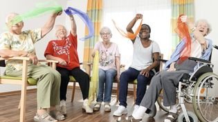 Fünf Frauen winken mit Tüchern und sitzen auf Stühlen.