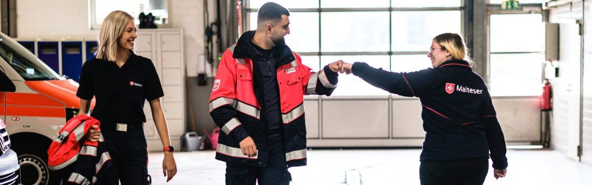 Junge, lächelnde Freiwillige der Malteser in Deutschland geben sich im Vorbeigehen einen Fistbump