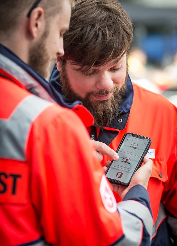 Zwei Männer im Sanitätsdienst schauen gemeinsam auf ein Smartphone.