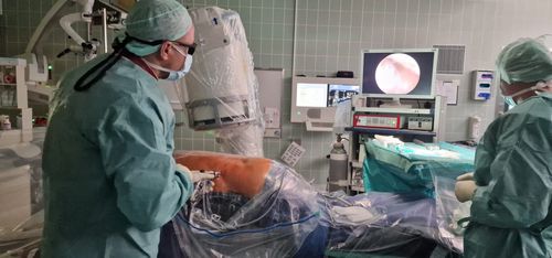 Operateur in steriler Schutzkleidung führt eine minimalinvasive Behandlung am Rücken unter Bildgebung im OP-Saal durch.