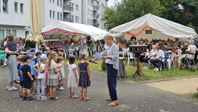 Eine Gruppe kleiner Kinder führt ein Programm auf. Senioren sehen zu.