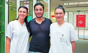 Zwei Pflegekräfte in Weiß und ein Mitarbeiter stehen nebeneinander vor dem Eingang einer medizinischen Einrichtung.