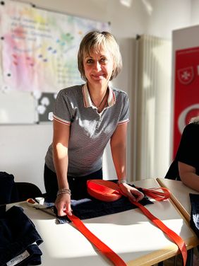 Eine Frau stehend und lächelnd am Tisch, auf dem Nähutensilien liegen.