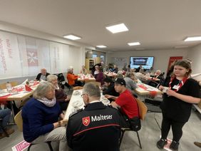 Das Bild zeigt den Ausbildungsraum der Malteser in Haltern am See, mit liebevoll gedeckten Tischen. Menschen sitzen an diesen Tische und lassen sich den Kuch schmecken.