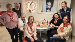 Die ehrenamtlichen Malteser sitzen und stehen um einen Tisch mit Kuchen und Süßigkeiten