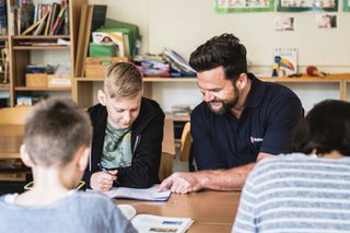 Malteser Schulbegleitdienst: Ein Malteser Mitarbeiter hilft einem Jungen beim Lesen.