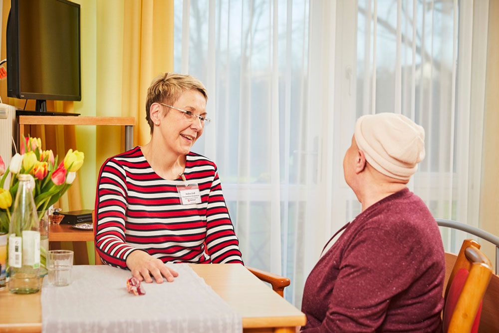 Mitarbeiterin der Malteser und Patientin sitzen am Tisch und unterhalten sich